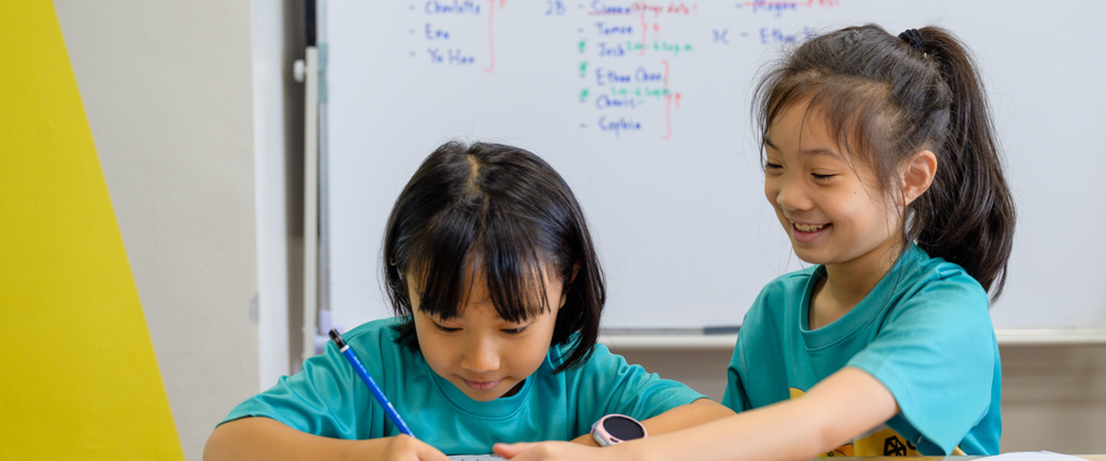 Two primary school children engaged in a guided learning activity at Agora Co-Learning @ Sixth Avenue, a Bukit Timah neighbourhood student care and enrichment centre offering after-school programmes for P1 to P6 students near Methodist Girls’ School, Raffles Girls’ Primary, Nanyang Primary, Pei Hwa Presbyterian, and Henry Park Primary.